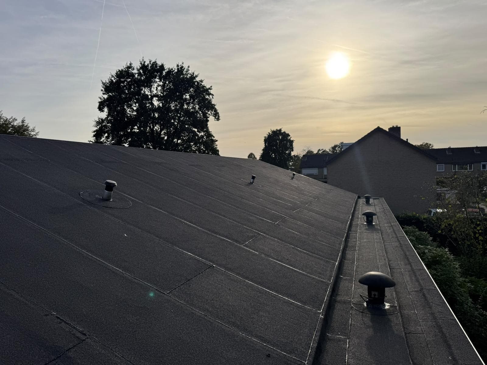 Groot hellend dak met nieuwe zwarte dakbedekking in de avondzon