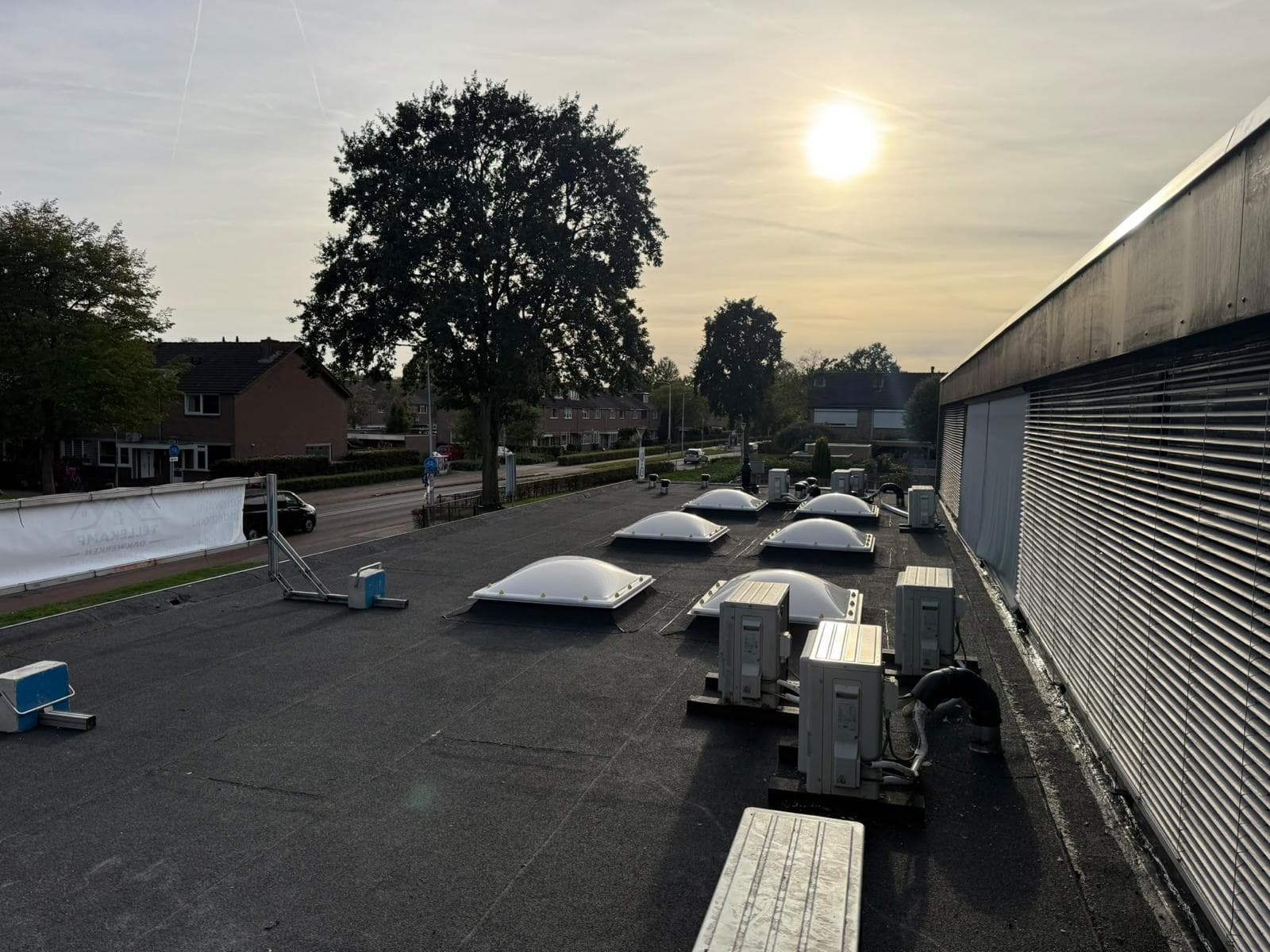 Plat dak met lichtkoepels en airco-units langs een gevel met zonwering